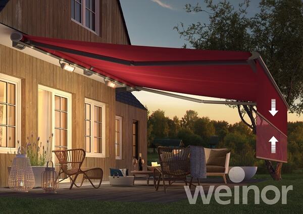 Moderne Terrassenüberdachung mit roter Markise an Holzhaus bei Sonnenuntergang.