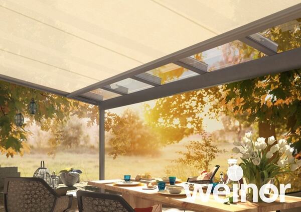 Überdachte Terrasse mit Glasdach und gemütlicher Sitzgruppe im Garten im Sonnenlicht.