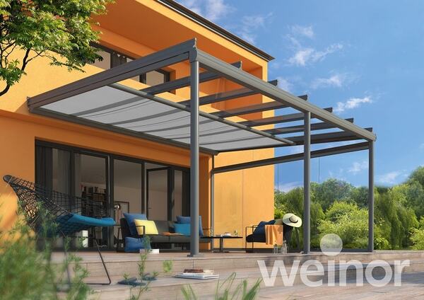 Moderne Terrassenüberdachung aus Glas und Aluminium an einem gelben Haus im Garten.